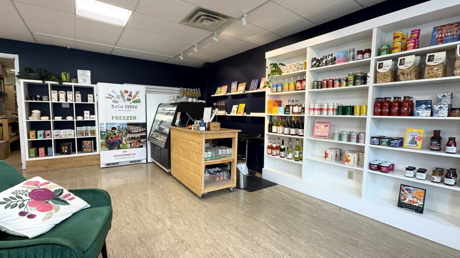 Inside The Pantry at Yellowknife Books: shelves of craft pantry goods, a cheese case, the Bush Order freezer and a wooden counter